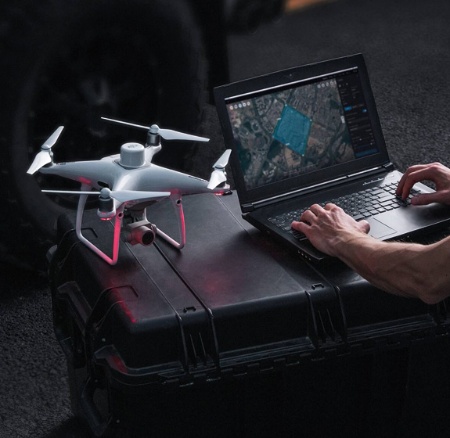 човек, използващ лаптоп, поставен върху сандък, а до него стои дрон