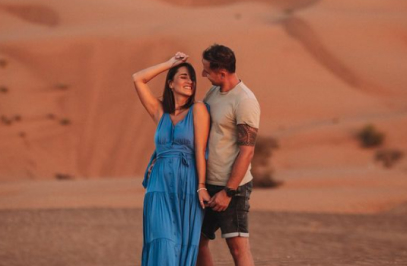 двойка в пустинята, която се държи за ръце и се усмихва един на друг