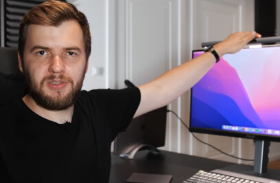 Мъж, който седи на бюро и държи монитор, обяснява на камерата какво прави.