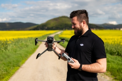 мъж, който стои в полето и държи дрон в ръката си