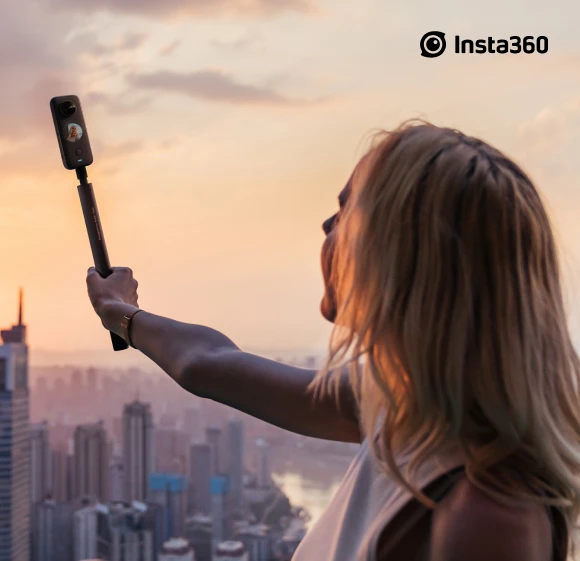 жена държи фотоапарат и си прави селфи на фона на голям град